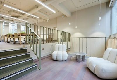 Relaxed break-out area featuring plush white armchairs and a modern staircase.