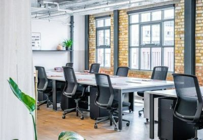 Workstations with black ergonomic chairs set against a backdrop of classic brickwork and large windows.