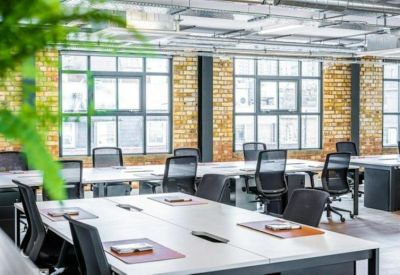Spacious open-plan workspace with multiple desks, black mesh chairs, and exposed brick walls.