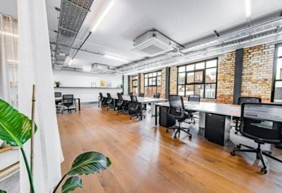Open-plan office area seen through a white curtain with leafy green plants and wooden flooring.