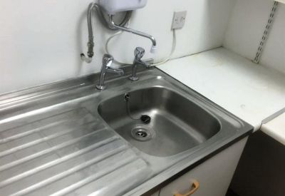 Small office kitchenette featuring a stainless steel sink and wall-mounted water heater.