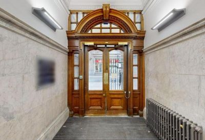 Grand building entrance featuring an arched wooden door and marble walls.