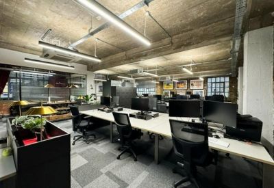 Industrial-style open-plan workspace with concrete ceilings, linear lighting, and large desks.