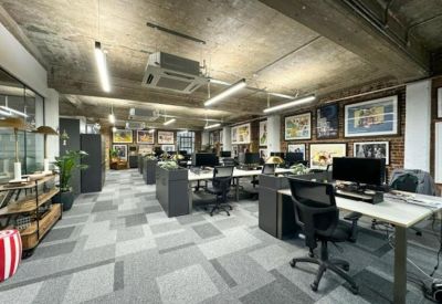 Spacious office interior with grey patterned carpet, framed wall art, and multiple workstations.