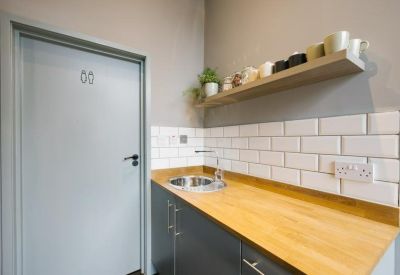 Bright kitchenette featuring a light wood countertop, white subway tiles, and a floating shelf with mugs.