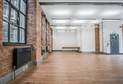 Spacious open-plan office with wooden flooring and exposed red brick walls.