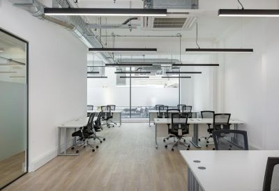 Bright open-plan workspace with multiple white desks, ergonomic chairs, and overhead linear lighting.