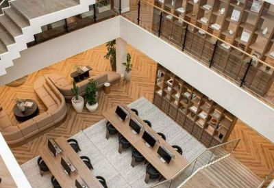 High-angle view of an open-plan coworking space with wooden chevron flooring and long work tables.