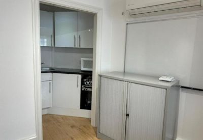 A doorway leading into a clean, modern kitchenette with white cabinetry and dark countertops.