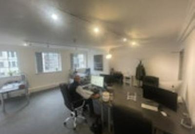 Open-plan office with desks, monitors, and an employee working under bright ceiling lights.