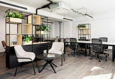 Modern breakout area with white armchairs, a black round table, and a plant-filled shelving unit.