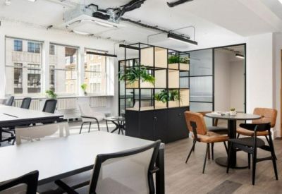 Spacious open-plan workspace with multiple white desks, black chairs, and natural light.