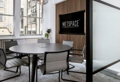 Meeting room with a round grey table, silver-framed mesh chairs, and a branded wall display.