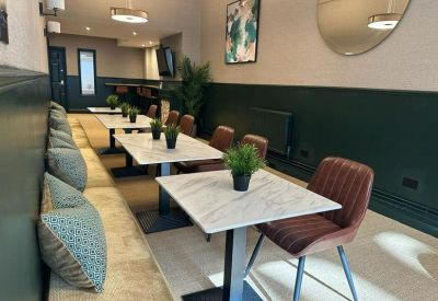 Long dining area featuring marble-topped tables, a green accent wall, and booth seating with patterned cushions.