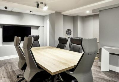 Sleek modern boardroom with a large light-wood table, grey executive chairs, and a wall-mounted screen.
