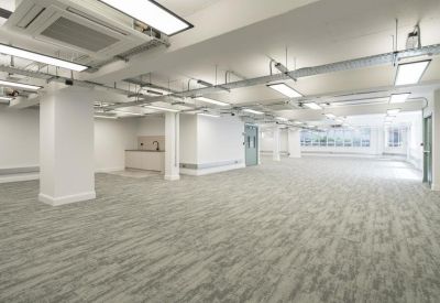 Large empty floor plate with industrial-style exposed ceiling pipes and white pillars.