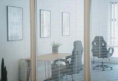 Private office viewed through horizontal blinds featuring modern workstations.
