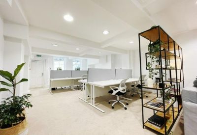 Open-plan office space with white desks, ergonomic chairs, and a black metal shelving unit.
