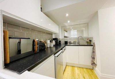 Modern white kitchen with black countertops and light wood flooring.