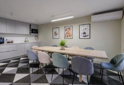 Modern communal kitchen and dining area with a long wooden table and colorful chairs.