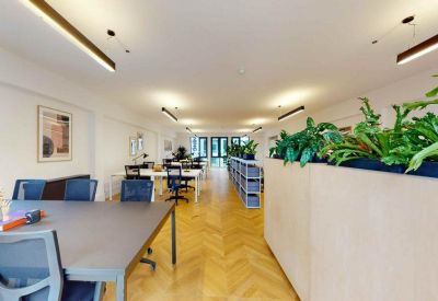 Spacious open-plan workspace with chevron wood flooring and overhead greenery.