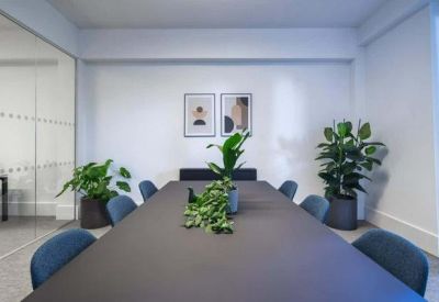 Professional meeting room featuring a grey conference table, blue chairs, and abstract art.