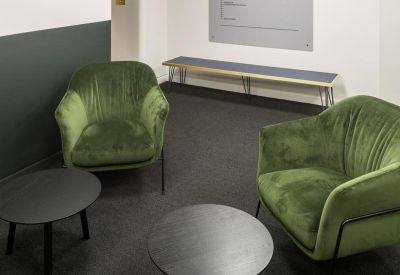 Communal lounge area featuring green velvet armchairs and round coffee tables.