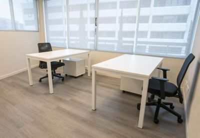 Bright two-person office suite with white desks and large windows with blinds.