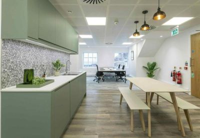 Modern office kitchen with sage green cabinetry and a light wood dining table with benches.