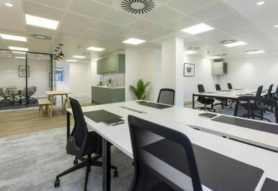Open-plan office with white desks, ergonomic chairs, and a kitchen area in the background.