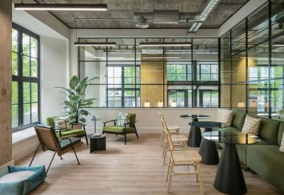 Spacious communal lounge and breakout area at Riley Studios featuring olive green sofas and industrial windows.