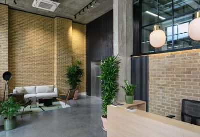Bright reception area featuring a wooden front desk, exposed brick walls, and tall indoor plants.
