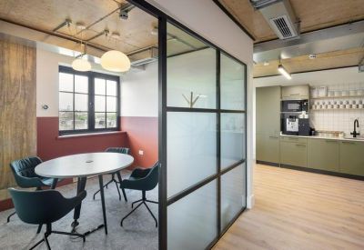 Small meeting room with a round table and dark chairs, partitioned by a glass and black steel wall.
