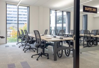 Glass-walled office suite with adjustable desks and city views through large windows.