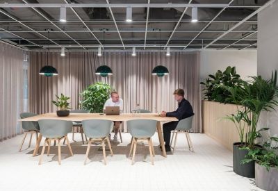 Modern meeting room with a light wood table, grey chairs, and a pink curtain backdrop.