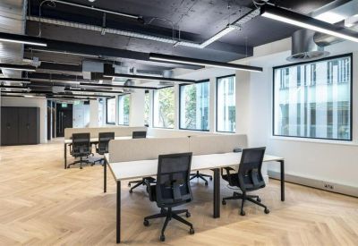 Spacious open-plan workspace with white desks, ergonomic black chairs, and large windows.