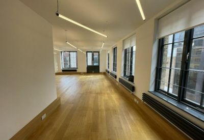Spacious open-plan office with wooden floors and linear pendant lighting.