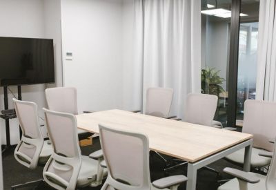 Professional meeting room with a light wood table, grey ergonomic chairs, and a large wall-mounted monitor.