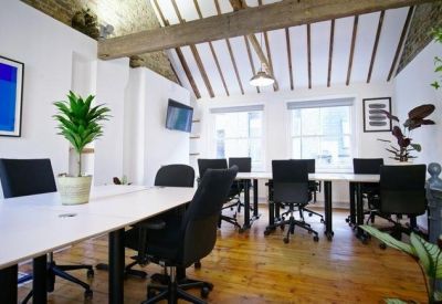 Sunlit open-plan office under a vaulted timber ceiling with white desks and green plants.