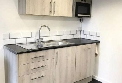 Modern communal kitchen with light wood cabinetry and integrated microwave.