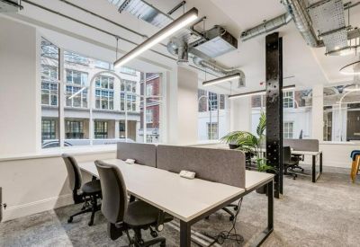 Open-plan office space with rows of white desks and industrial-style ceiling ductwork.