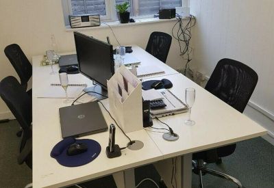 Open-plan office with white desks, black ergonomic chairs, and garden views.