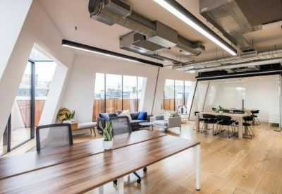 Bright open-plan office with wooden floors and exposed ceiling ducts.