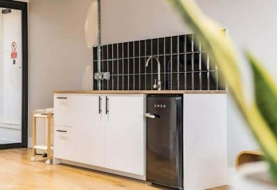 Sleek office kitchenette with white cabinetry and a black tiled backsplash.