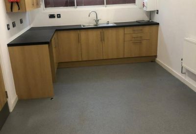 Modern communal kitchen with wooden cabinetry, black countertops, and a grey floor.