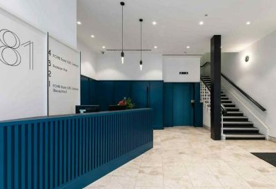 Reception lobby with a blue slatted desk, white walls, and a prominent staircase.