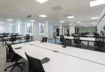 Spacious open-plan office with rows of white desks and ergonomic black chairs.