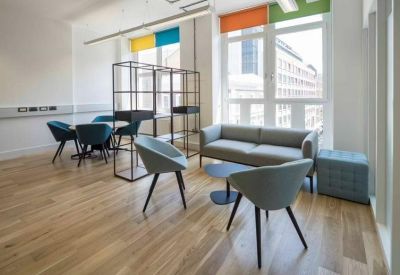 Bright communal lounge with a grey sofa, teal chairs, and colorful window accents.