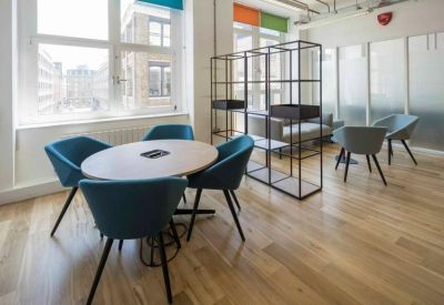 Meeting area with a round table and teal upholstered chairs next to large windows.