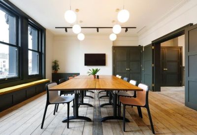 Large wooden boardroom table in a bright room with black-framed windows and modern lighting.